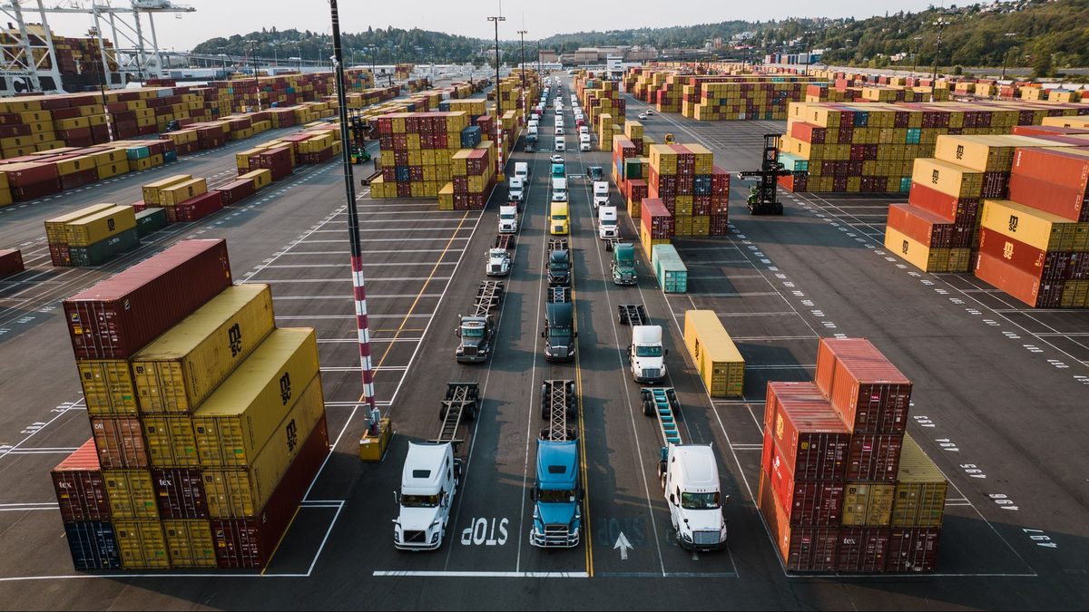 Camiones de drayage en fila dentro de una terminal de contenedores, donde aplican los vales de camión eléctrico para drayage en Port Newark