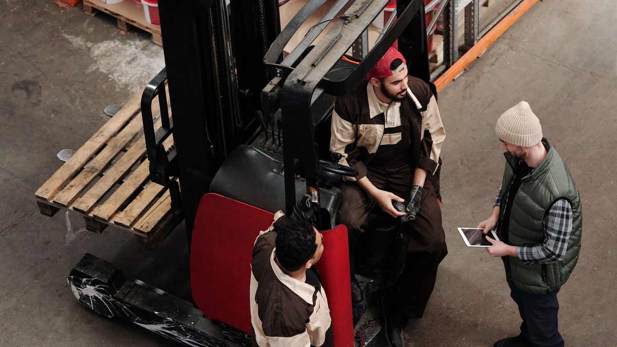 Warehouse crew reviewing a tablet beside a forklift — verify new motor carrier authority and insurance before you tender